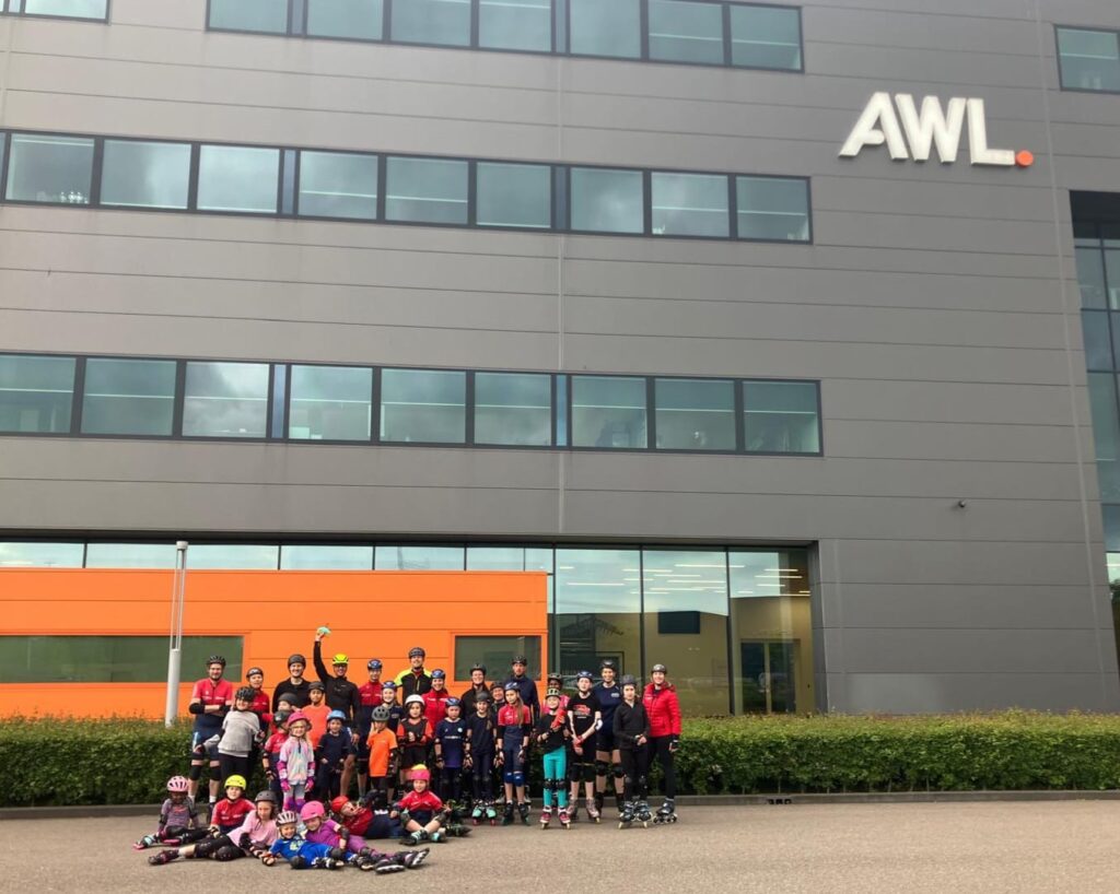 Training bij AWL: groepsfoto van jeugd en volwassenen op skeelers voor het bedrijfspand
